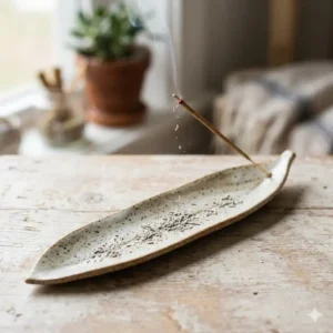 A long leaf-shaped handmade incense holder effectively catching falling ash from a lit incense stick.