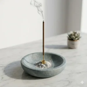 A functional grey stone incense burner stick holder catching falling ash from a burning stick.