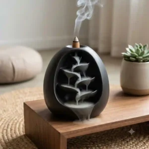 A modern black ceramic large incense burner with a burning cone creating a cascading smoke waterfall effect for meditation.